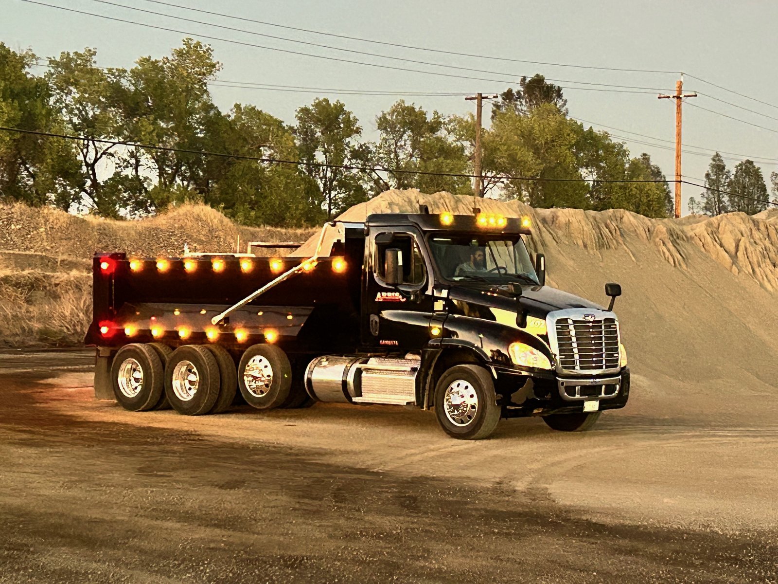 Black dump truck with its lights on at a gravel site