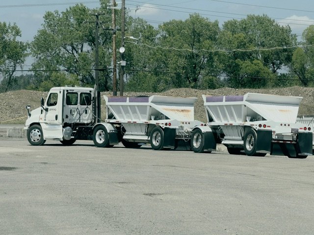White tractor pulling double bottom-dump trailers