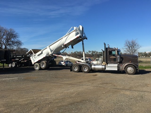 End-dump trailer tipped up behind a tractor in the yard