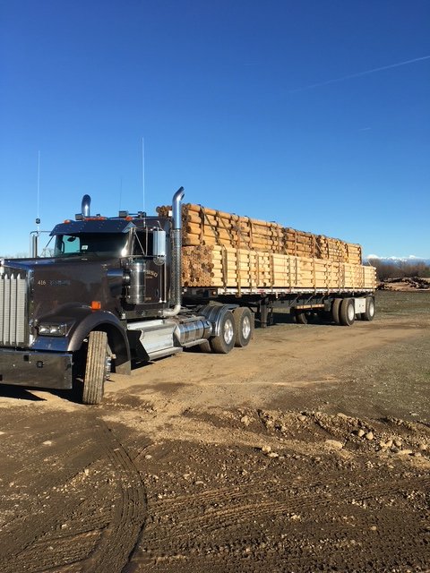 Tractor with a flatbed trailer loaded with lumber on a dirt lot