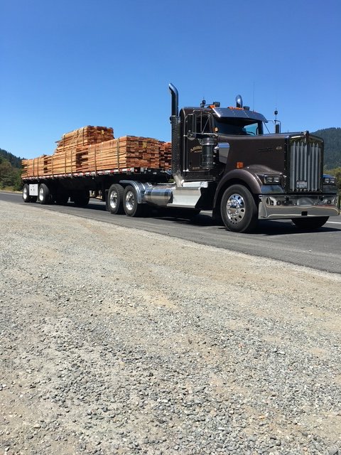 Tractor with a lumber load on a flatbed trailer, parked by the road